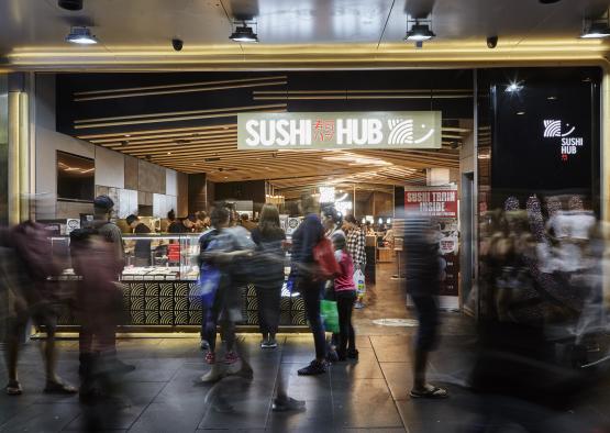 a group of people standing in front of a sushi hub