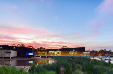 a building with a body of water and a pond with a pink and blue sky