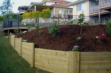 a wooden fenced hillside with plants and a fenced yard